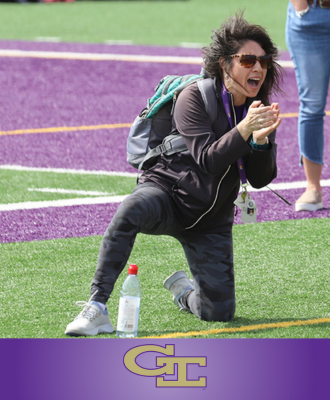  GISH Unified Track Coach, Andrea Hill, cheering on competitors while kneeling on the turf. 